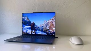 The Lenovo Yoga Slim 7x running Assassin's Creed: Valhalla on a white desk next to a gray gaming mouse